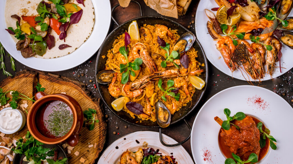 Spanish dishes including seafood paella, grilled seafood platters, and other traditional Spanish delicacies served on a rustic table.