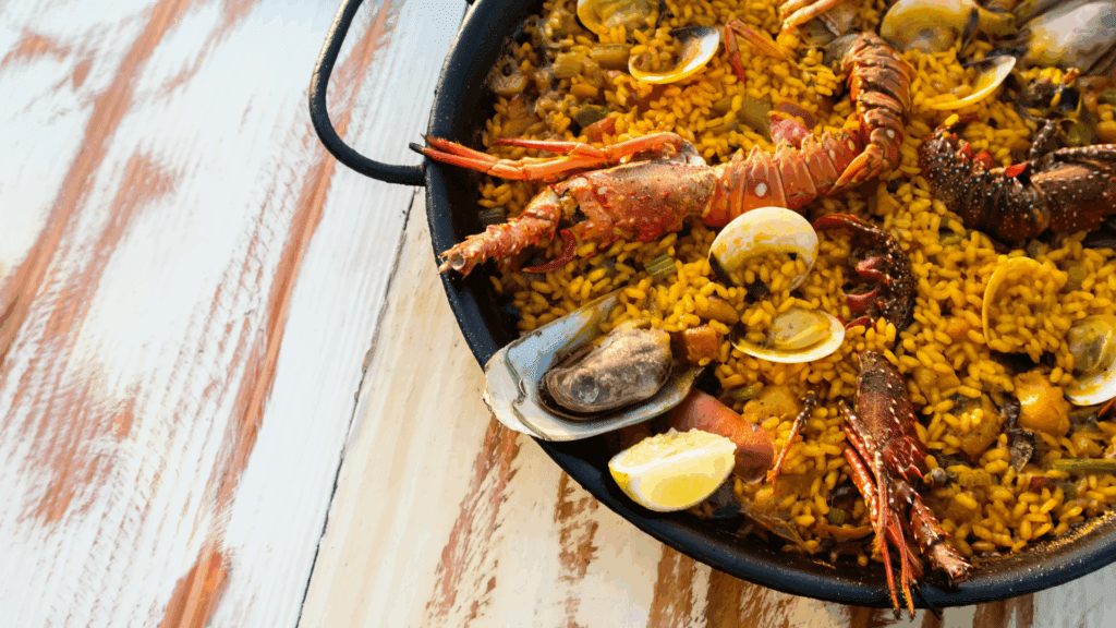 Traditional Spanish seafood paella served in a large pan, featuring lobster, mussels, clams, and vibrant saffron rice