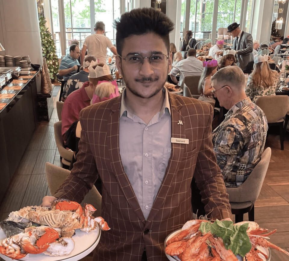 Swanand, a participant of the Intern & Trainee Program, serving seafood dishes in a busy restaurant setting.
