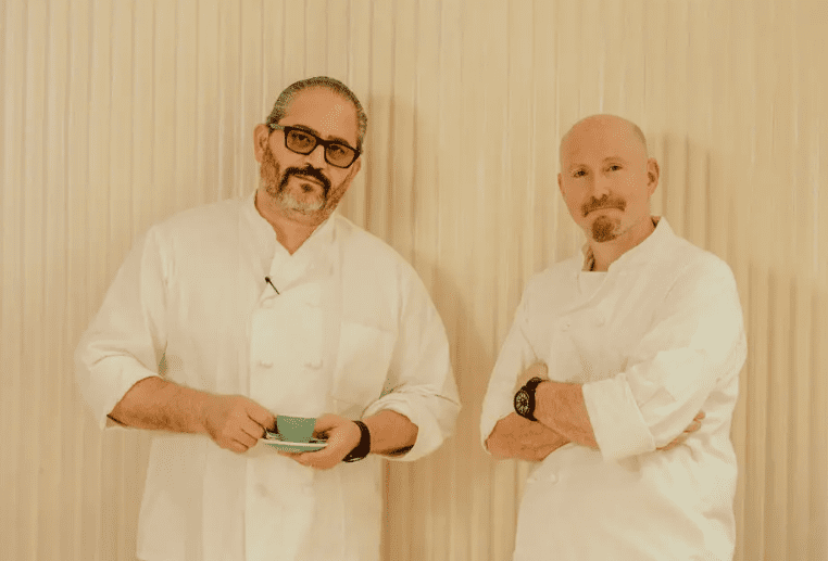 Two professional chefs, Lee Hanson and Riad Nasr, standing in white coats, showcasing leadership in global cuisine.