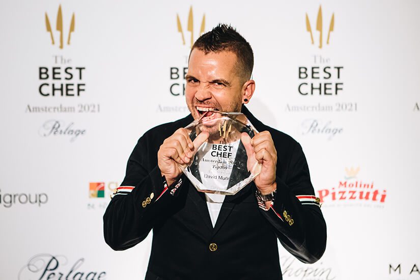 Chef Dabiz Muñoz holding and playfully biting his Best Chef Award trophy, celebrating his recognition among the best chefs in the world.
