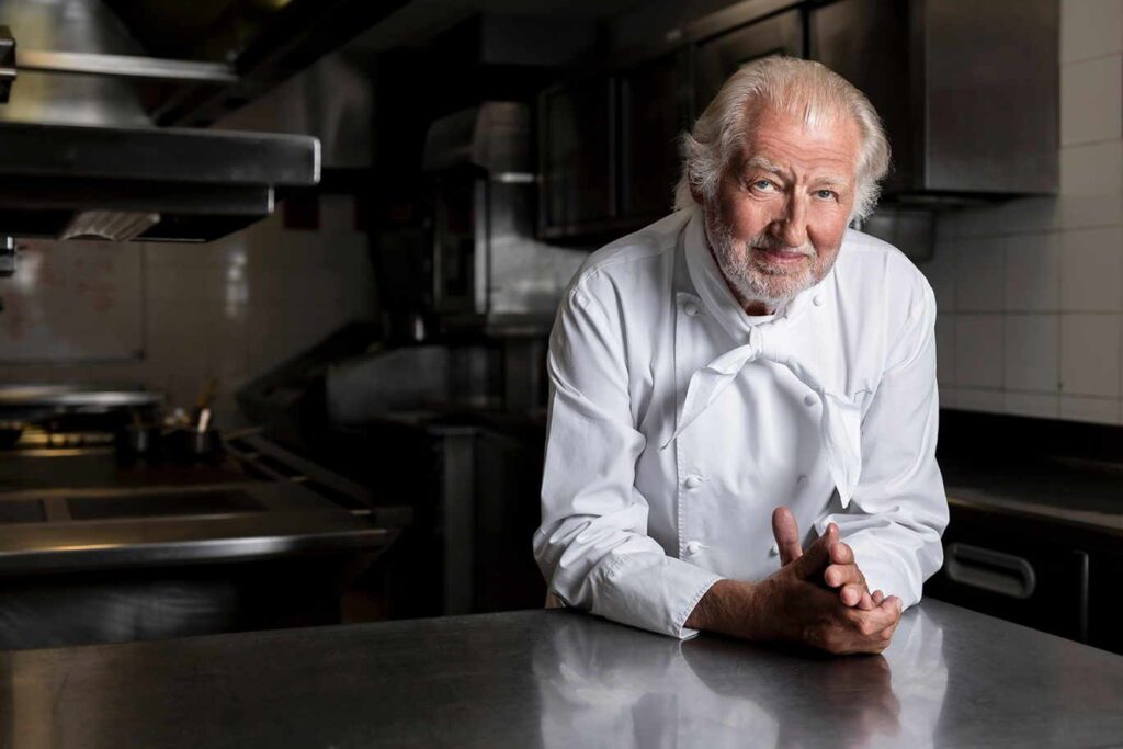 Michelin-star chef in a white uniform leaning on a kitchen counter, exuding confidence and culinary mastery.